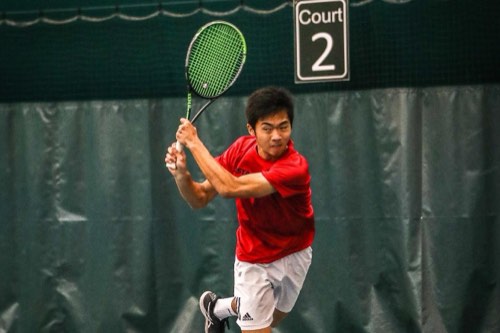 Albert finishing a one-handed backhand on an indoor court