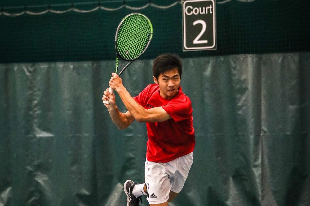 Albert finishing a one-handed backhand on an indoor court